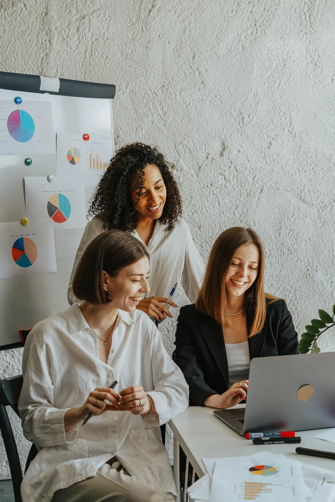 Trois femmes souriantes travaillant ensemble devant un ordinateur portable et des graphiques