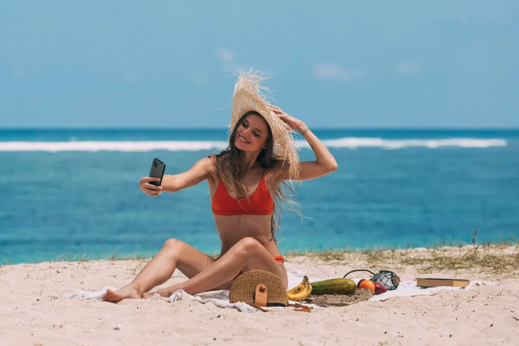 Gérer ses réseaux sociaux l'été sans s'épuiser : le cahier de vacances de ta com 3 Femme prenant un selfie sur la plage en été