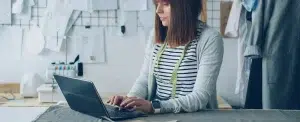 Une couturière écrit sa newsletter sur son ordinateur portable dans son atelier