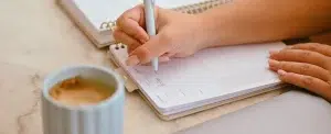 Une indépendante note son plan d’action dans son agenda, un café à côté