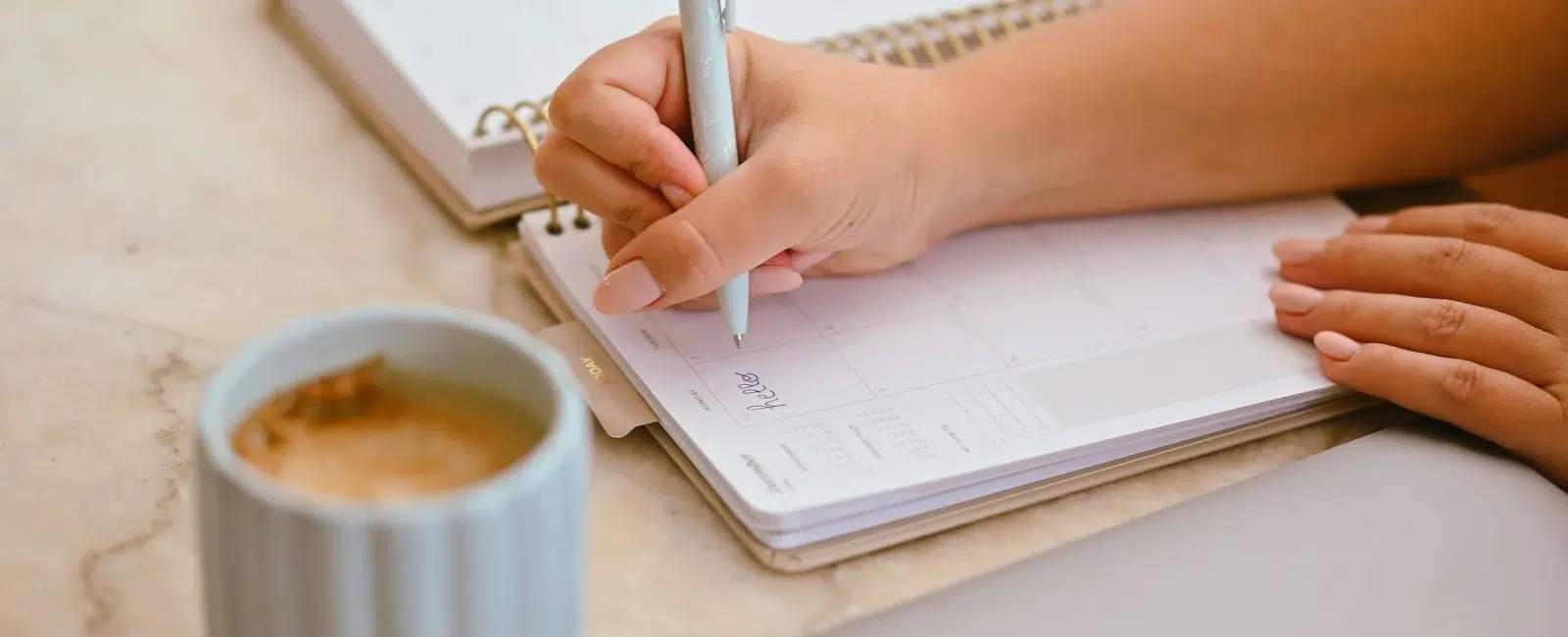 Une indépendante note son plan d’action dans son agenda, un café à côté