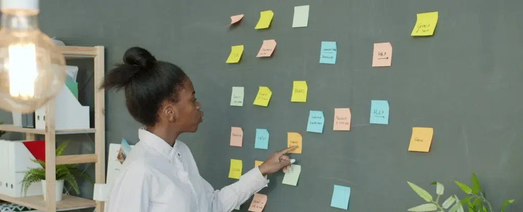 Stratégie de communication digitale : 6 décisions et un exemple complet 8 Une entrepreneuse organise les post-it de sa stratégie de communication sur un mur